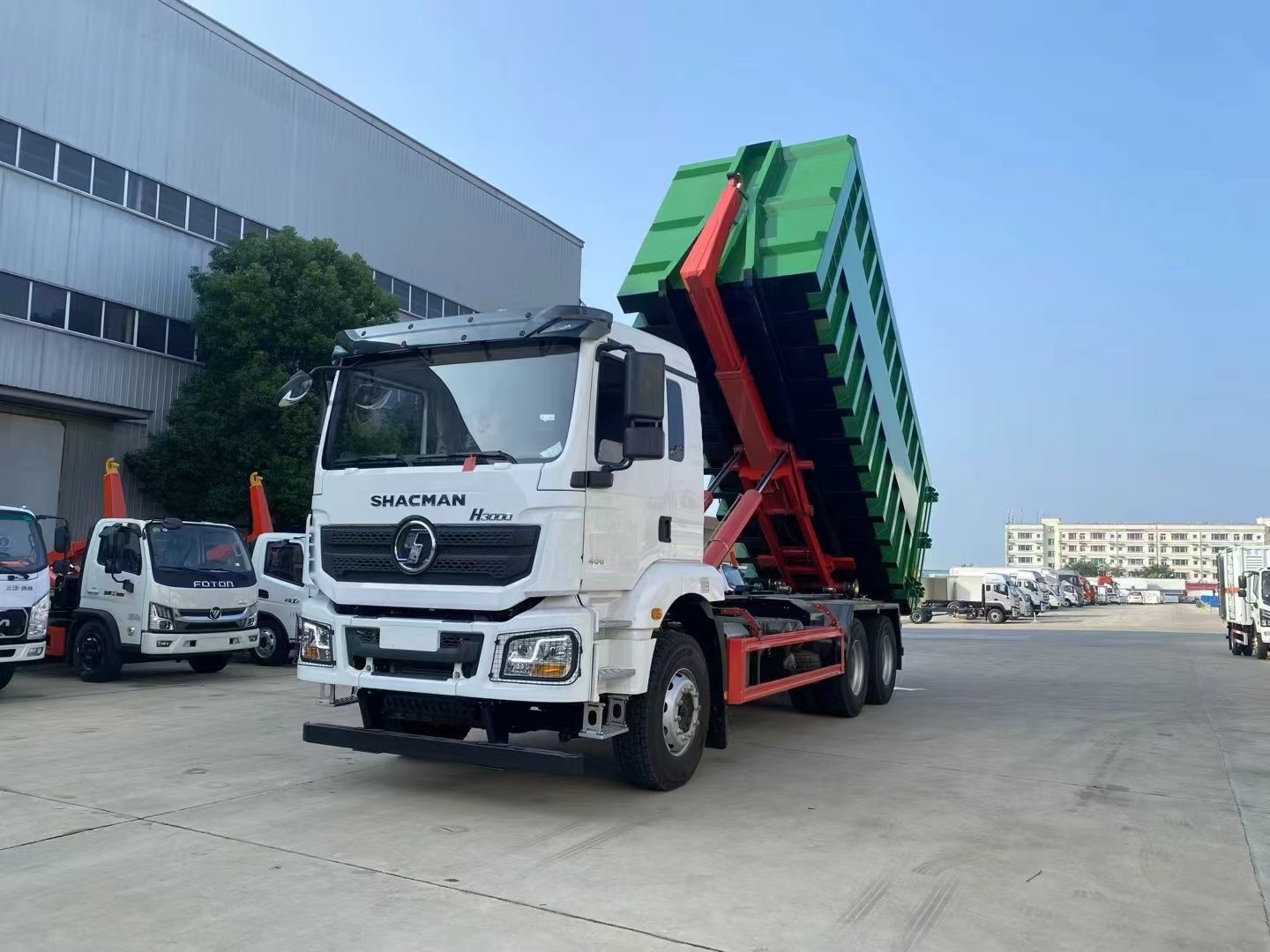 White SHACMAN H3000 hook-lift truck raising a green waste container