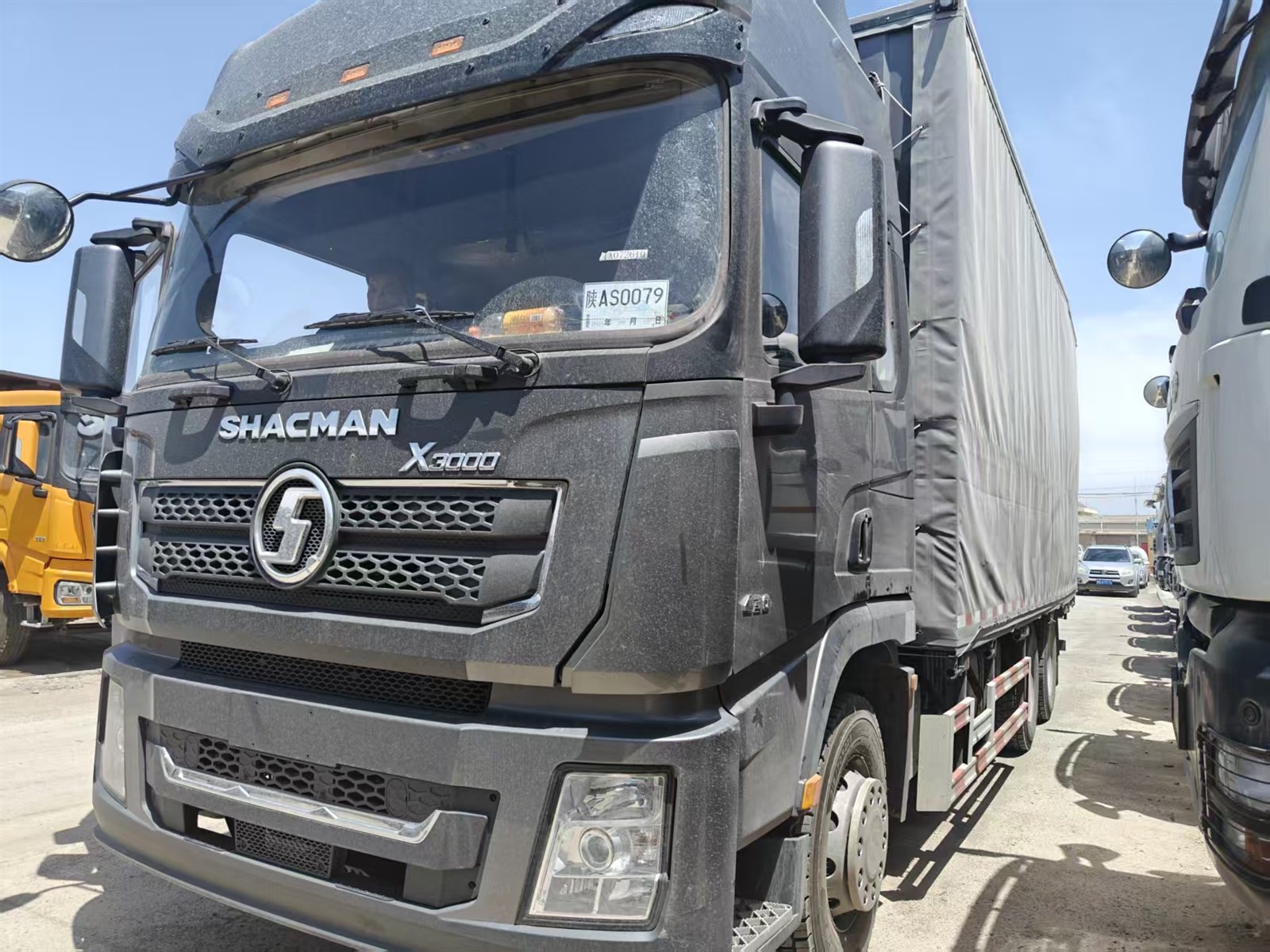 Black SHACMAN X3000 curtain-side cargo truck in a vehicle yard