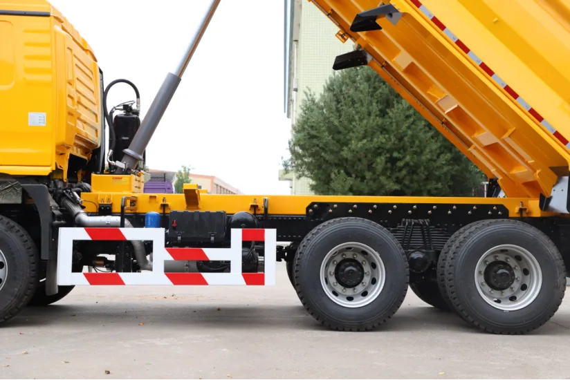 Raised SAGMOTO X5 dump body showing hoist, frame and tandem rear axles